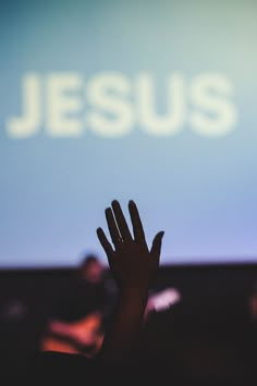 someone holding their hand up in front of a screen with the word jesus on it