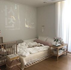 an unmade bed sitting in the middle of a living room next to a baby crib