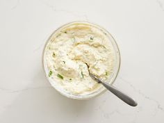 a glass bowl filled with cream cheese and a spoon on a white table top next to it