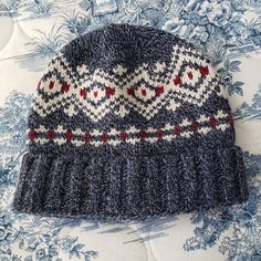 a knitted hat sitting on top of a blue and white tablecloth covered bed