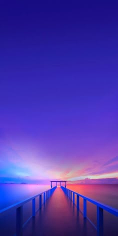 a long pier stretches out into the ocean at sunset with blue and purple hues