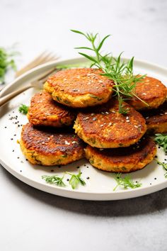 a white plate topped with crab cakes and garnished with green herbs next to chopsticks