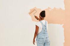 a woman in overalls painting a wall with a paint roller