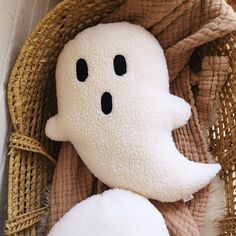 a white stuffed ghost in a basket on the floor next to a brown and tan blanket