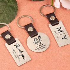 three personalized key chains are shown on a pink surface next to a white flower