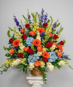 a basket filled with lots of flowers sitting on top of a white pedestal next to a wall