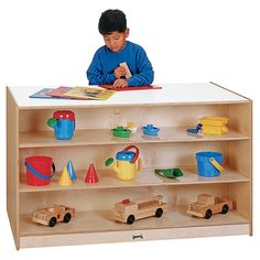 a young boy sitting at a table with toys in front of him and reading a book