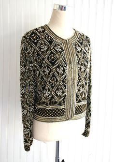 "This is a VERY heavily beaded cocktail party jacket.  There are some missing pearls along the neckline and down the front.   It is otherwise in beautiful conditon.  Marked size L 44\" total bust 17\" shoulder  19 1/2\" nape to hem  Purveyor's Note: We have searched far and wide, wrestled bears, braved the cold, traversed mountain ranges, fought pirates, swam with sharks and eaten at many a questionable road side taco stand to provide our customers with one of a kind vintage pieces.  Know that whichever piece you choose to make your own has its own story and has traveled through time to get to you.  Though we strive to provide the absolute best, \"pristine\" vintage pieces are rare birds, if not altogether non-existent.  That being said, please understand that part of buying and wearing vi Elegant Fitted Hand Embellished Outerwear, Elegant Embroidered Party Outerwear, Glamorous Beaded Outerwear For Evenings, Elegant Beaded Festive Outerwear, Beaded Winter Outerwear For Formal Occasions, Elegant Hand Embellished Long Sleeve Outerwear, Elegant Long Sleeve Hand Embellished Outerwear, Beaded Evening Outerwear For Winter, Formal Beaded Winter Outerwear