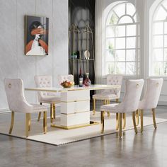 a white and gold dining table surrounded by beige upholstered chairs in front of a large window