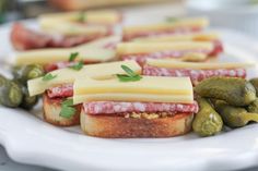 sandwiches with cheese, meat and olives on a white plate next to pickles