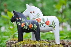 two wooden horses painted with flowers on them in the grass and trees behind them are bushes