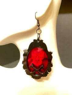 Get ready for Halloween with these eye-catching Sugar Skull and Crossbones Framed Earrings! Crafted from red mirrored acrylic and black acrylic, the laser engraved sugar skull design and laser cut frame with crossbones make for a striking and unique accessory. Show off your gothic style and add an edgy touch to any outfit with these must-have earrings! Each earring is made with 2 layers of 3MM acrylic, but are VERY LIGHT WEIGHT!French hook with silicone stoppers. Earrings are 2" X 1.5" long. *** Gothic Red Jewelry For Halloween, Red Gothic Jewelry For Halloween, Red Punk Earrings For Gifts, Spooky Red Halloween Jewelry, Red Novelty Jewelry For Halloween, Red Pierced Halloween Earrings, Red Pierced Earrings For Halloween, Nickel-free Red Halloween Jewelry, Red Nickel-free Jewelry For Halloween