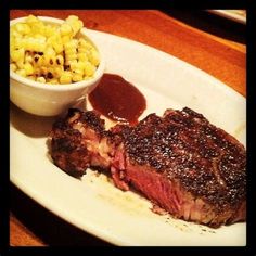 steak, macaroni and cheese on a white plate with a small bowl of sauce