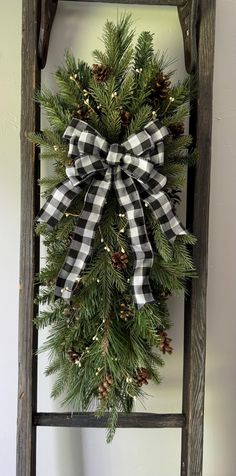 a christmas wreath hanging on an old wooden ladder with pine cones and evergreens tied to it