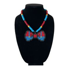 This handmade necklace showcases a charming Mario bow tie design with vibrant beads. It's perfect for adding a pop of color to your festival or party outfit. The necklace features a tie closure and is made with high-quality materials to ensure durability. The brand, Byte Size Kandi, is known for its unique and creative jewelry designs. This necklace will make a great addition to any jewelry collection and is a must-have for any fan of Mario Kandi Necklace, Bow Tie Design, Beaded Jewelry Necklaces, Rave Party, Tie Design, Kandy, Fuse Beads, Creative Jewelry, Handmade Necklace