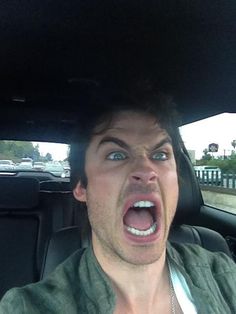 a man in a car with his mouth open and tongue out, making an angry face