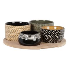 four bowls on a wooden tray with black, white and gold designs in them sitting next to each other