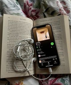 an open book with headphones attached to it laying on a bed next to a cell phone