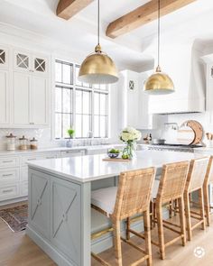 a large kitchen with white cabinets and wooden flooring, two pendant lights hanging over the island