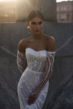 a woman in a white dress standing next to a stone wall with her hands on her hips