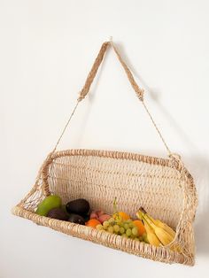 a wicker hanging basket filled with assorted fruit on a white wall behind it