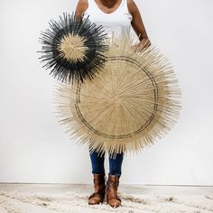 a woman standing in front of a white wall holding an umbrella made out of straw