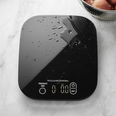 an electronic scale sitting on top of a white counter next to a bowl of apples