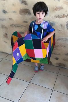 a little boy standing next to a colorful paper cut out of a horse on the floor