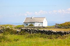 a small white house sitting on top of a lush green field next to a stone wall