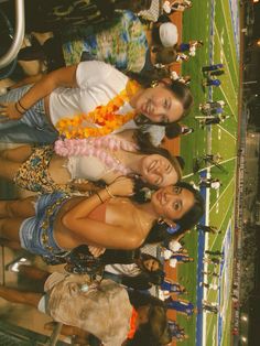 three young women standing next to each other in front of a crowd at a football game