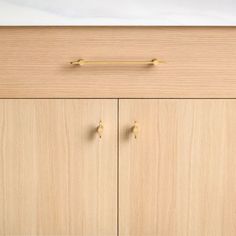 a wooden cabinet with two brass handles and knobs on it's doors, in front of a white wall