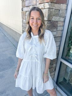 Add a touch of elegance to your wardrobe with the Chic Moment Eyelit Bow Tier Dress in white. This dress features delicate eyelit detailing and a charming bow, making it the perfect choice for any occasion. You'll feel confident and lovely in this stylish and sophisticated piece! Ashlyn is wearing a size small, which is her typical size for dresses! White Eyelet Mini Dress For Day Out, White Mini Dress With Bow For Day Out, White Broderie Anglaise Mini Dress For Day Out, Feminine Eyelet Dress For Day Out, White Eyelet Dress For Day Out, White Eyelet Mini Dress Feminine Style, White Eyelet Mini Dress With Short Sleeves, White Eyelet Short Sleeve Mini Dress, White Short Sleeve Mini Dress With Eyelet Details