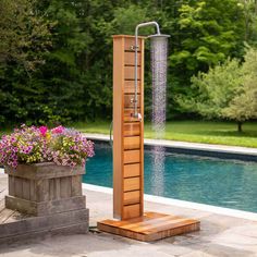 an outdoor shower in front of a swimming pool with flowers and potted plants on the side