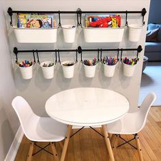 two white chairs and a table with some books on the wall behind them, in front of a children's book shelf