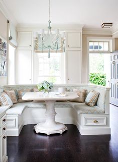 a kitchen with white cabinets and a table in the center, surrounded by built - in seating