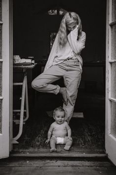 a woman standing next to a baby sitting on the ground