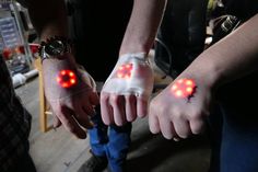 two hands with wristbands that have red lights on them, and one has an eyeball in the middle