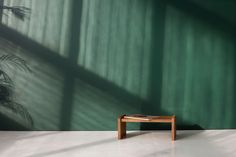 a small wooden bench sitting in front of a green wall with shadows on the walls