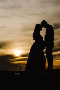 the silhouette of two people standing next to each other in front of a cloudy sky