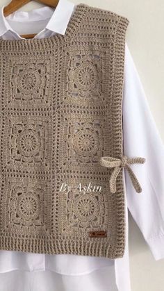 a crocheted sweater hanging on a wooden hanger next to a white shirt