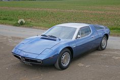 a blue sports car is parked on the side of the road in front of a field