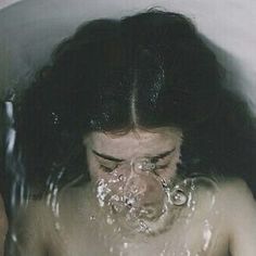 a woman is taking a bath in a white tub with water coming out of her mouth