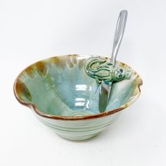 a ceramic bowl with a spoon in the shape of a frog on it's side