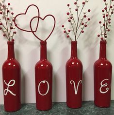 three red wine bottles with love written on them, one is empty and the other has flowers in it