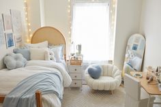 a bedroom with a bed, chair and desk in front of a large window that has string lights on the windowsill