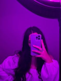 a woman taking a selfie with her cell phone in front of a purple light