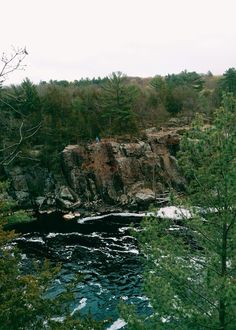 a river flowing through a lush green forest filled with lots of rocks and trees next to a cliff