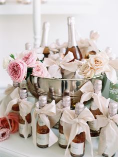 several bottles of wine and flowers in a silver bowl on a table with ribbons around them