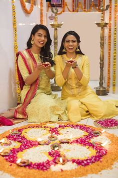 two women sitting next to each other in front of a flower decoration on the ground