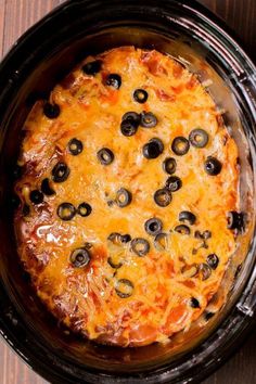 a casserole with olives and cheese in a crock pot on a wooden table